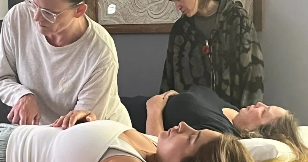 Two practitioners rest their hands gently on two people lying on their backs with eyes closed during Reiki practice