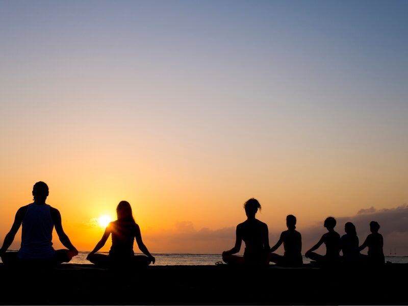 Silhouettes of a group meditating cross-legged on a beach at sunset