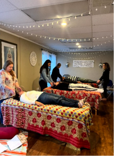Students practising Reiki on clients lying on treatment tables beneath string lights in the Ferndale studio