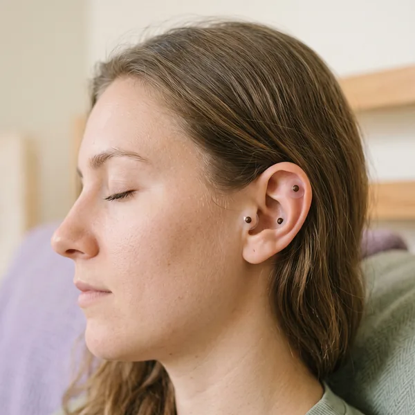 Side view of a woman with her eyes closed and three tiny seeds held on her outer ear by clear round dots